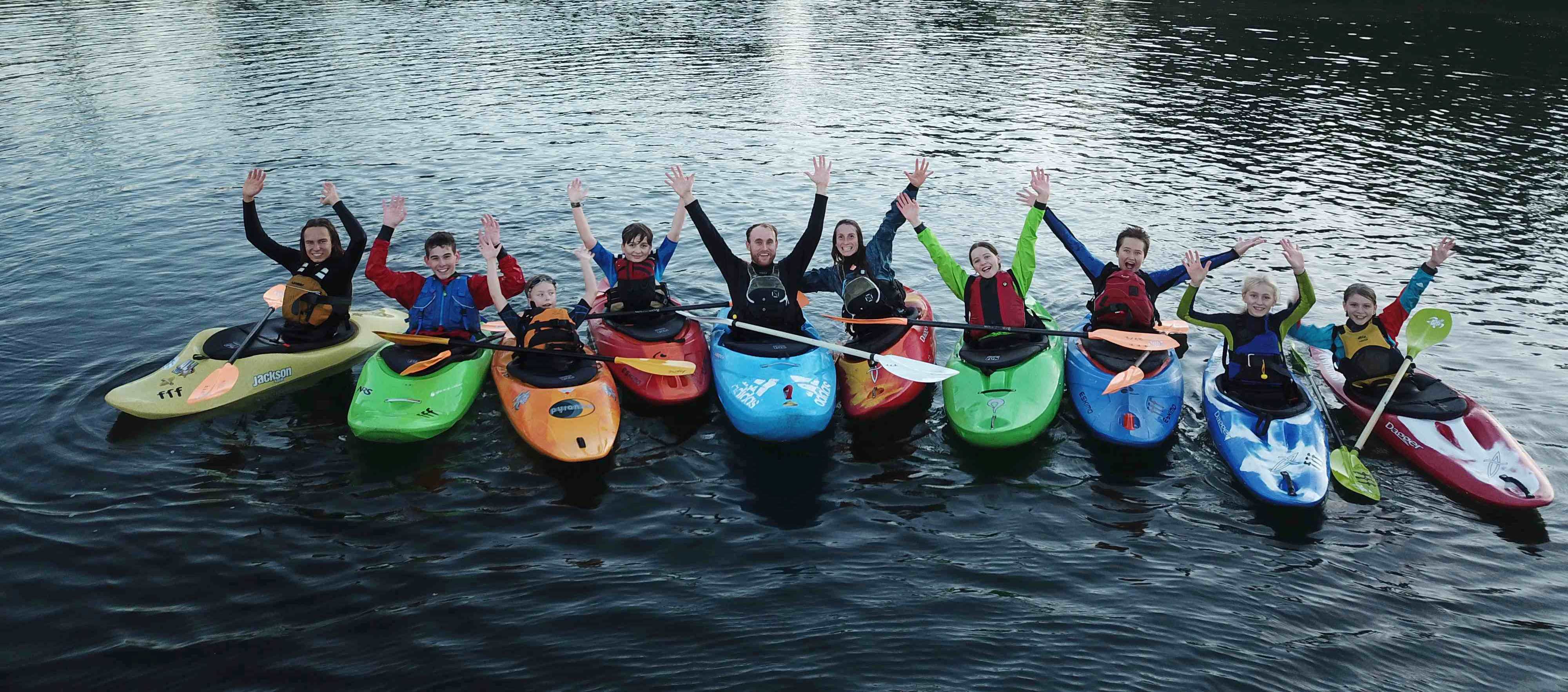8 Jugendliche mit Ihren Jugend-Trainern Jessi & Phil positionieren ihre Kajaks zu einem Gruppenbild nebeneinander - begeisternd für den Kanusport strecken sie lachend die Hände hoch