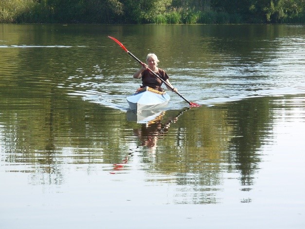 Eine Kanutin paddelt auf den ruhigen Rheinauen - im Wasser spiegeln sich die Bäume des Ufers