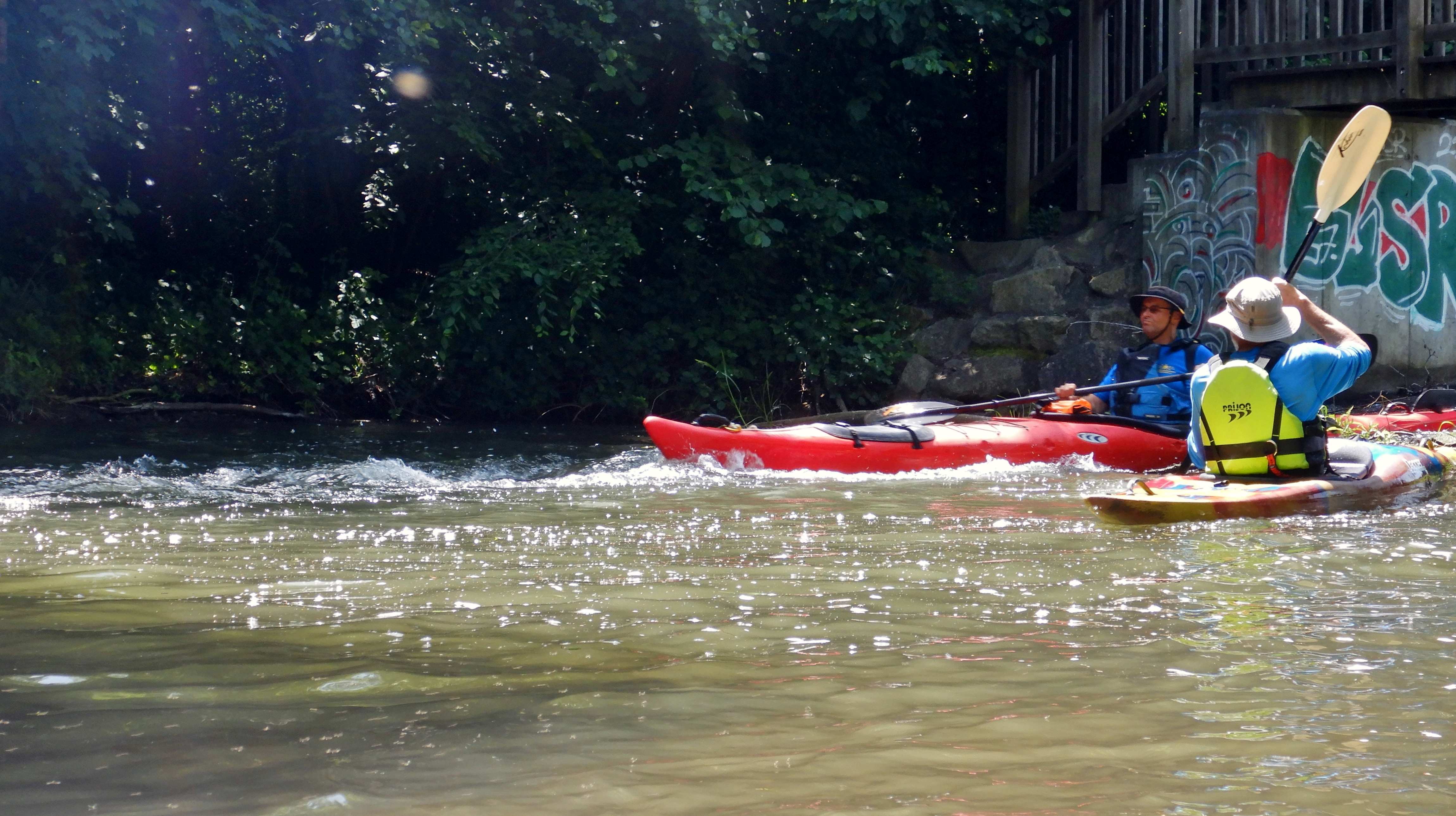 Ein kleiner Schwall erfreut die Kanuten: ein Paddler ist bereits gut durchekommen und wartet hilfsbereit im Kehrwasser. Ein weiterer Kanuten mit einem roten Seekajak meistert die Schwellen perfekt.