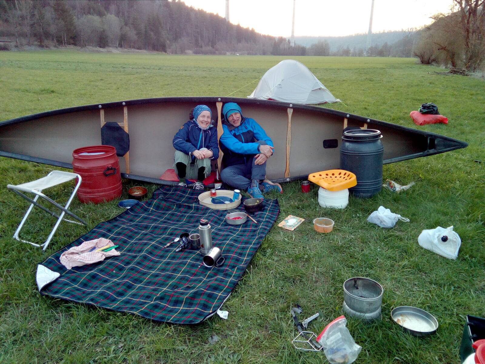 Gemütliches Paddlerlager bei einer Gepäckfahrt: Das Zelt ist aufgeschlagen und die Paddler sitzen windgeschützt an einer Mauer